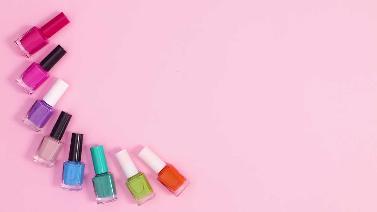 las botellas de esmalte de uñas de manicura aparecen en el lado izquierdo del fondo rosa pastel.