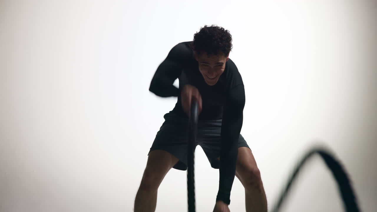 Determined Man Exercising with Battle Ropes in a Studio