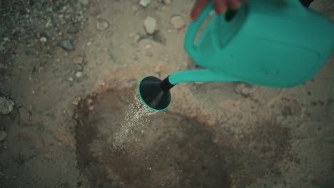 persona pobre irrigando un terreno desértico árido y arenoso con una olla de riego