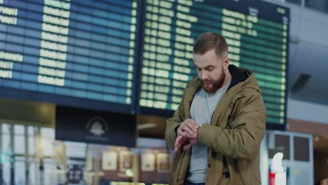 Young-Guy-With-A-Beard-Arriving-From-A-Trip-To-The-Airport-And-Walking-Through-The-Arrival-Hall,-Then-Young-Pretty-Girlfriend-Meeting-Him-And-Hugging-Tight