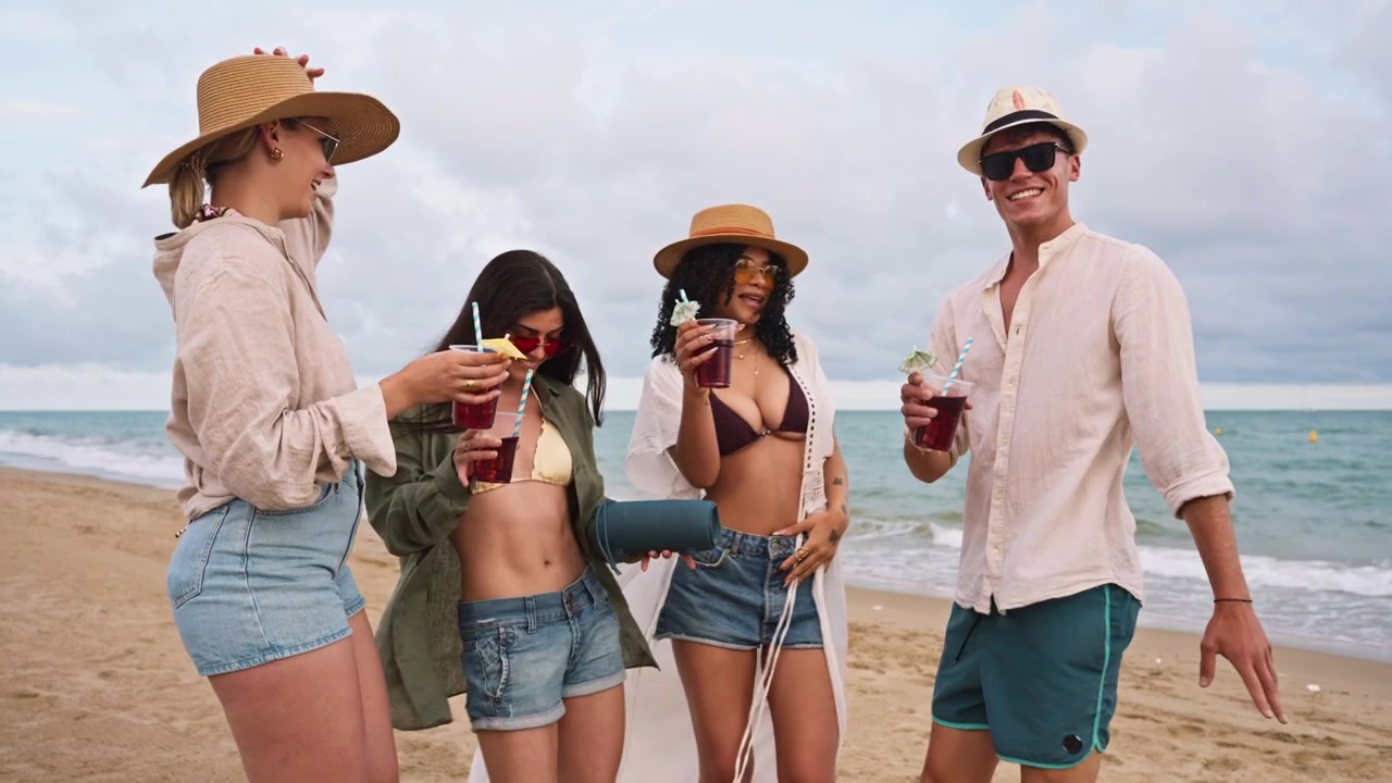 Giovani amici felici che si godono drink e musica in spiaggia