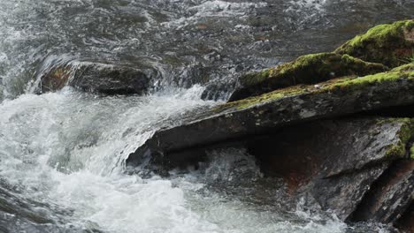 A-wild-river-rushes-and-cascades-over-dark-rocks-within-a-narrow-riverbed,-showcasing-the-untamed-power-and-rugged-beauty-of-nature's-waterways