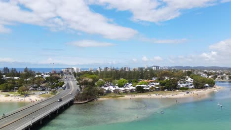 the tallebudgera creek bridge with vehicles passing by - tourists enjoying at the beautiful beach in burleigh heads, qld - ascending drone shot