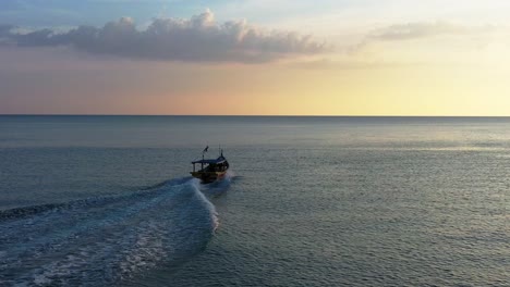 Cinematic-landscape-view-of-a-traditional-fishing-boat-sailing-on-andaman-sea-at-beautiful-sunset-golden-hour,-aerial-tracking-shot