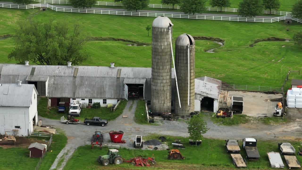 Historic old farmstead with silo storage, barn and machinery. Parking cars and tractor on field. Aerial view. River in background. Aerial approaching shot.