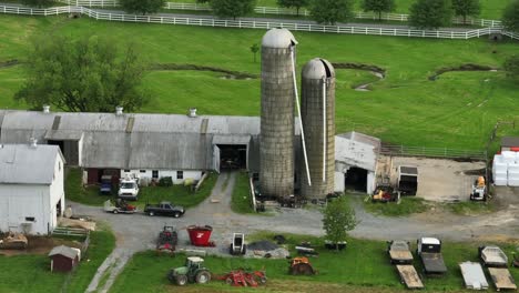 historic old farmstead with silo storage, barn and machinery. parking cars and tractor on field. aerial view. river in background. aerial approaching shot.