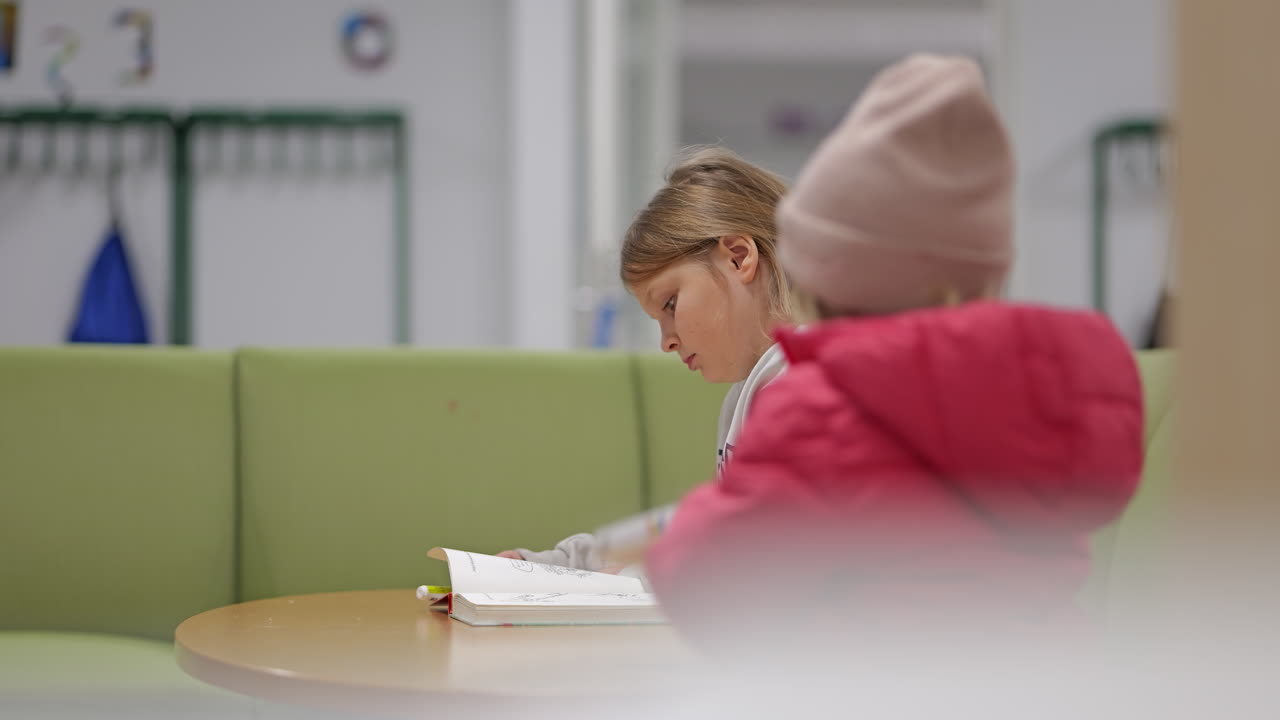 молодая девушка читает книгу в школьной библиотеке с зелеными диванами и спокойной атмосферой