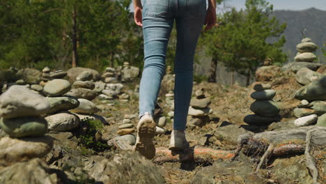 tourist walks across glade with stacked rocks to pine wood