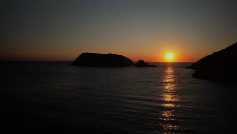 Setting-sun-bright-yellow-orange-glow-spreads-across-shimmering-ocean-wave-water,-syros-greece