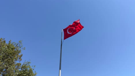 Die-Türkische-Flagge-Weht-Lebhaft-Im-Wind-Am-Fahnenmast-Vor-Dem-Klaren-Blauen-Himmel