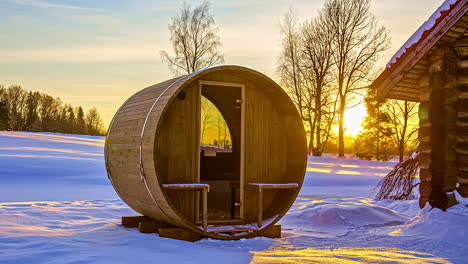 thermowood barrel sauna next to wooden cabin with bright sunset in background