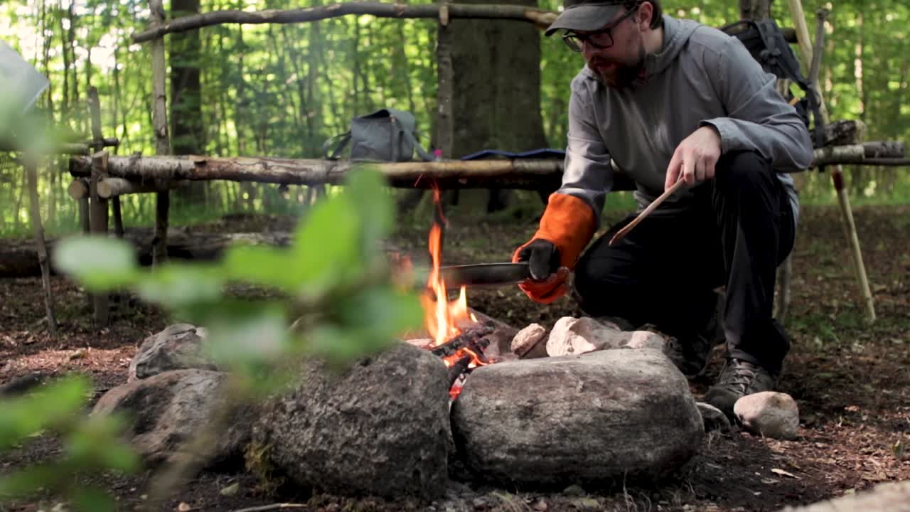 Man kookt steaks boven een rokend kampvuur in het zomerse bos.