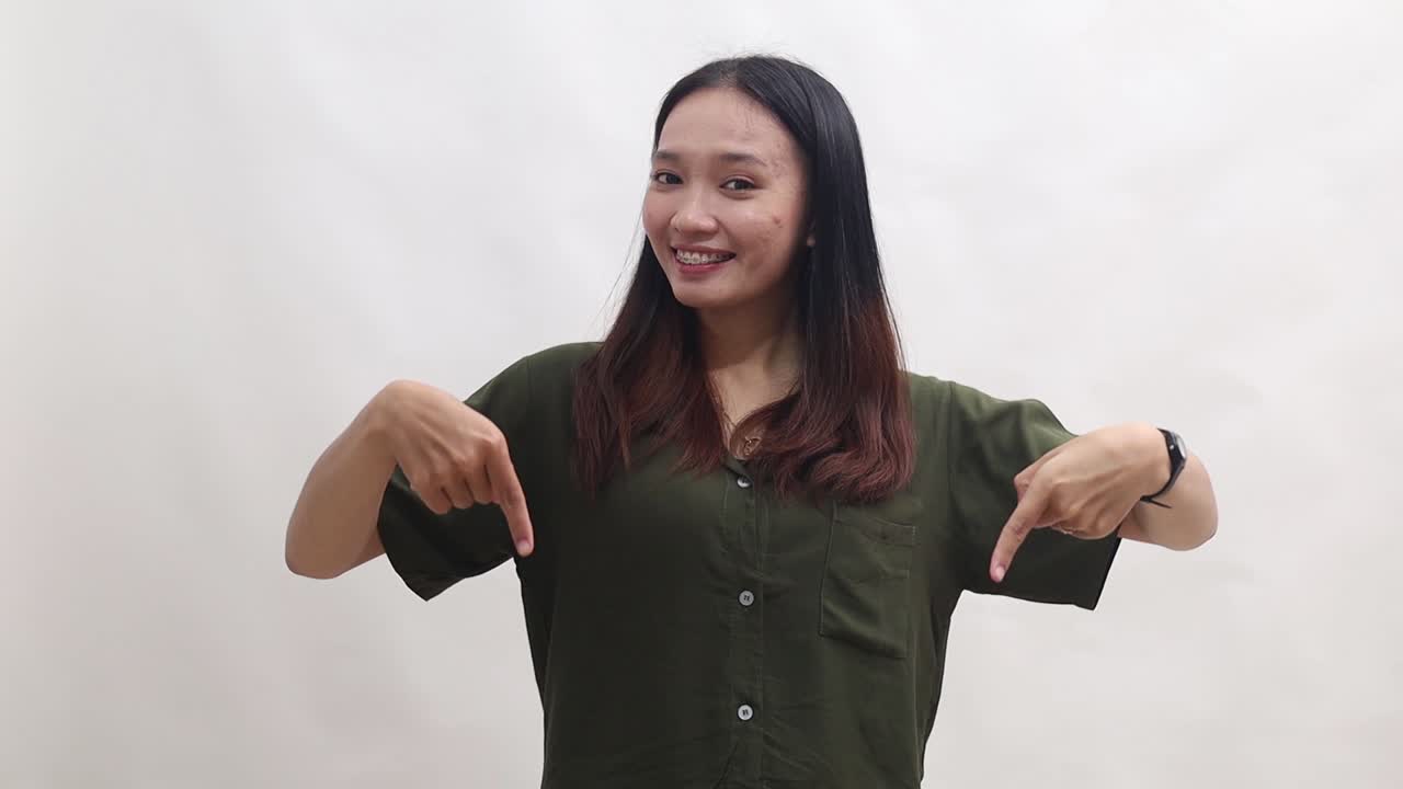 Smiling happy young Asian woman pointing fingers down on workspace area copy space mock up isolated on white background