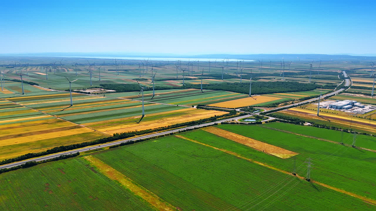 Picturesque countryside with green and yellow fields. Multiple wind turbines are scattered by the scenery