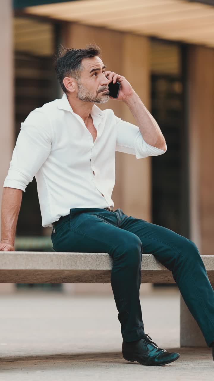 Uomo in camicia bianca seduto che parla al telefono