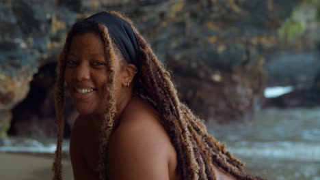 primer plano de una chica con rastas sonriendo y el océano en el fondo