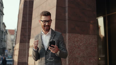 stylish man listening music on the smartphone via earphones while walking and dancing joyfully in the street 2