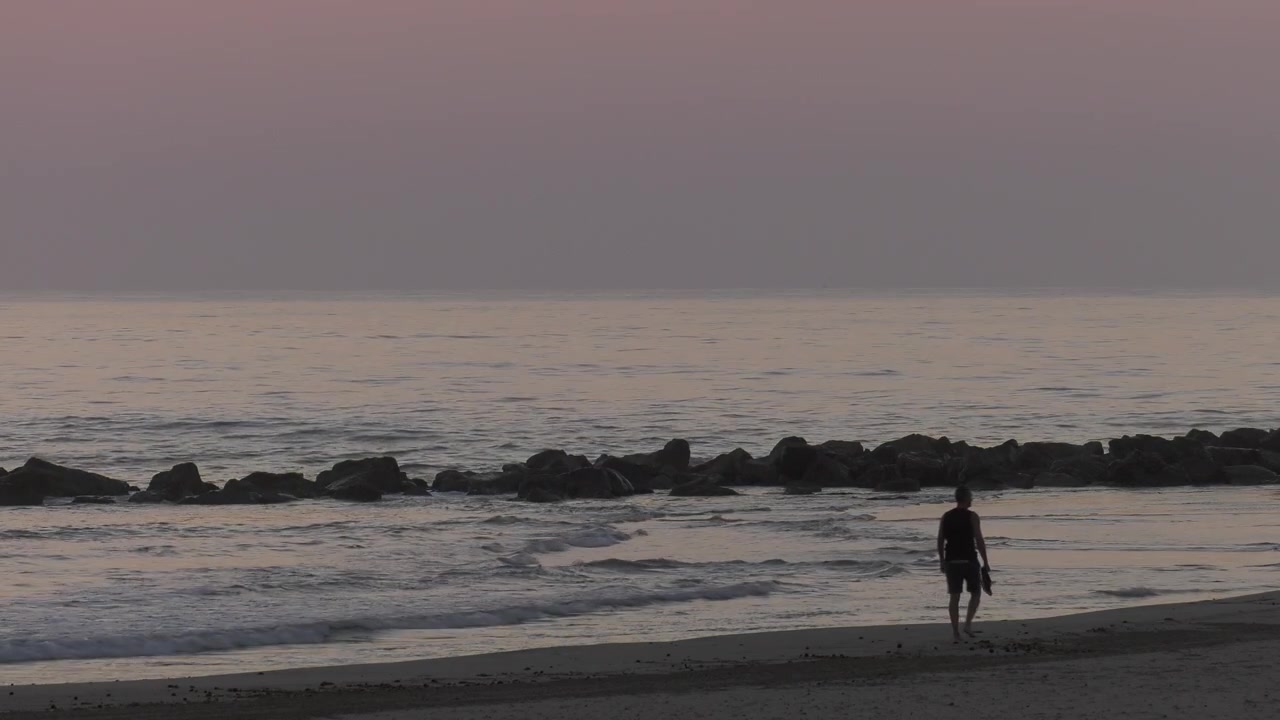 Uomo che cammina a piedi nudi sulla riva sabbiosa all'alba, silhouette