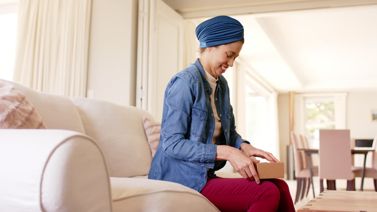 feliz mujer biracial en hijab desempaquetando cajas en casa, espacio de copia, cámara lenta