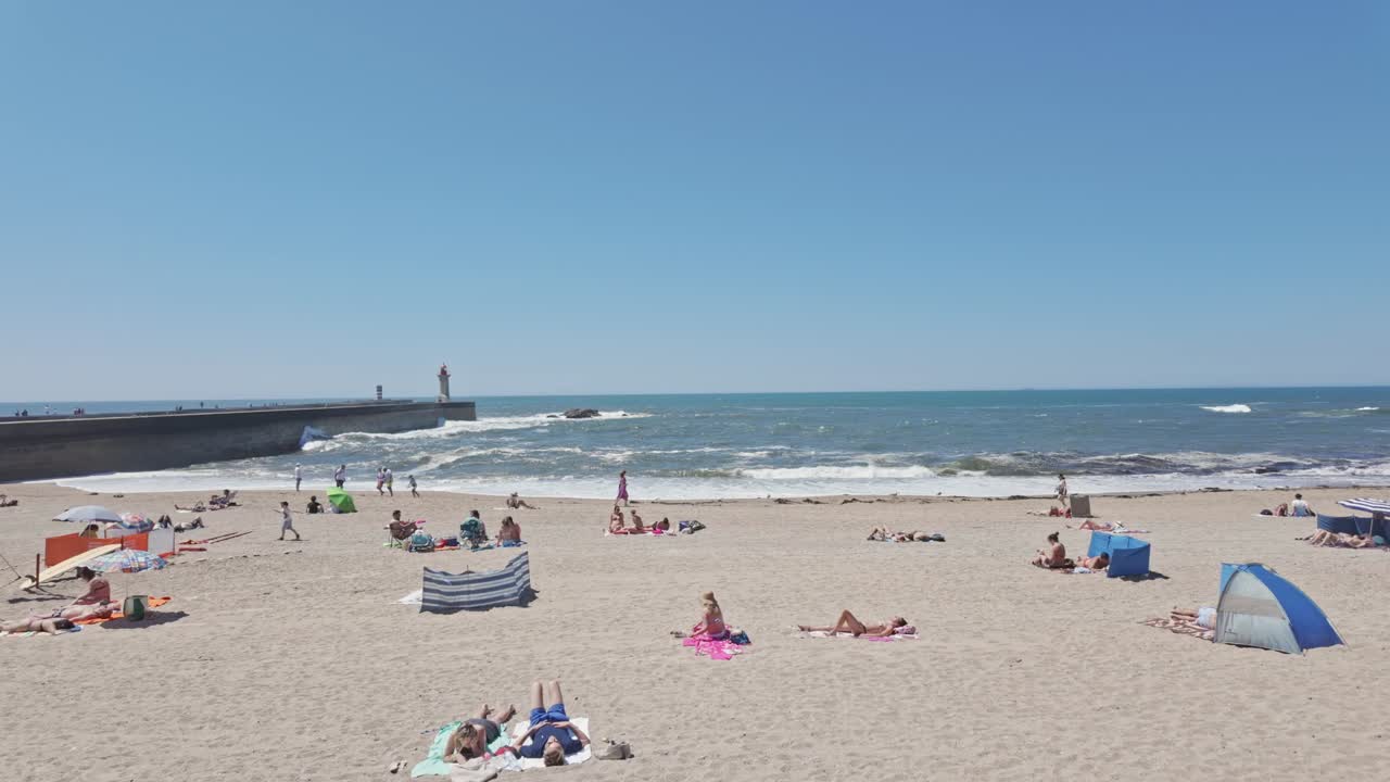 People walk along Praia do Carneiro beach promenade on a sunny day in Porto