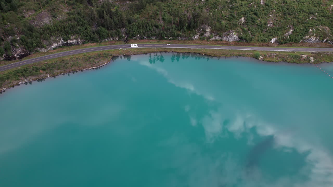 푸른색, 초록색, 투르코이즈색 호수의 해안에 있는 시골 도로의 놀라운 공중 전망, 드론이 몇 대의 자동차를 따라가고 있습니다. 노르웨이, 스칸디나비아의 물 위의 아름다운 반사