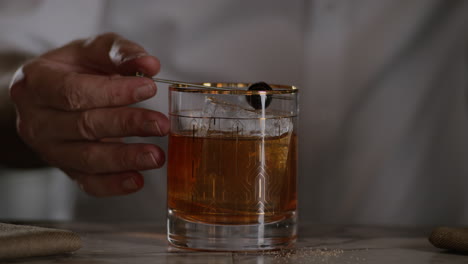 bartender garnishes an old fashioned with a maraschino cherry