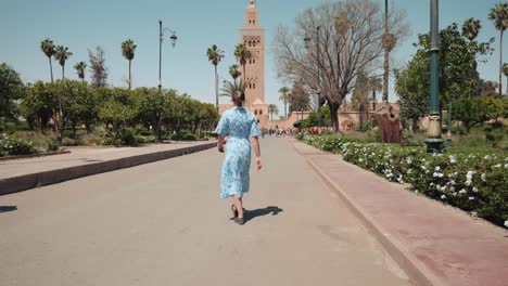 Una-Joven-Caucásica-Vestida-Caminando-Hacia-La-Mezquita-Koutoubia,-Marrakech,-Marruecos