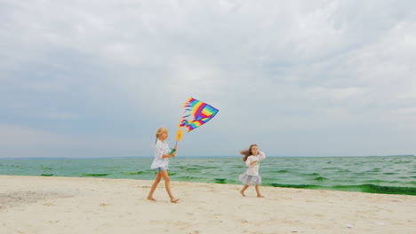 Two-Children-Playing-With-A-Kite-On-The-Beach-Against-Blue-Sky-Background
