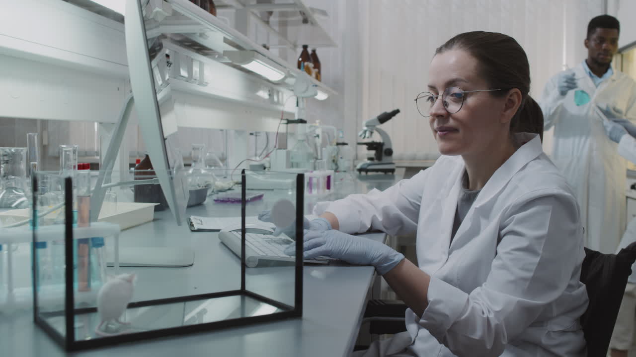 Female Scientist Observing Lab Rat and Typing on Computer