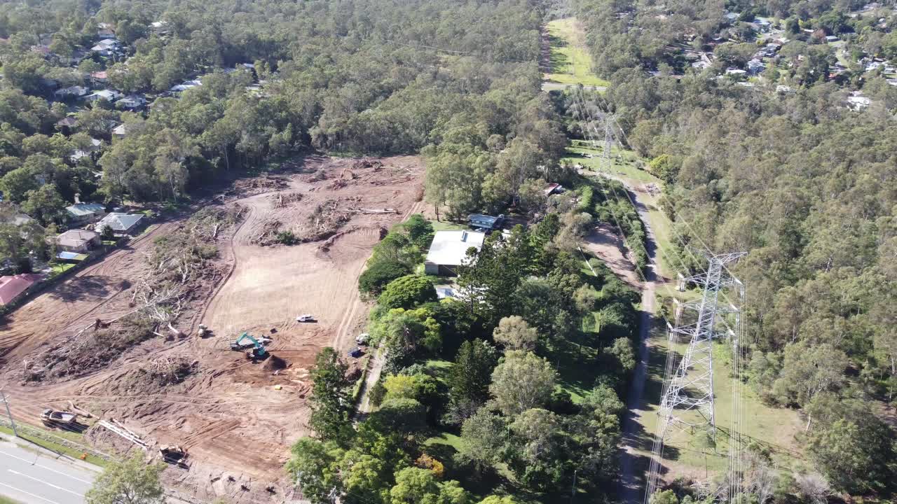 4K Aerial view of bushland being cleared by heavy machinery near a high voltage powerlines and near a residential suburb in Australia
