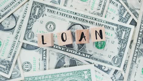 rotating word loan from wooden letters, on dollars, concept