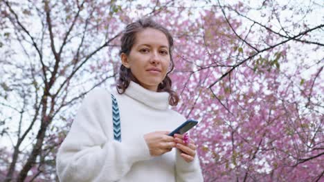woman using phone under cherry blossoms