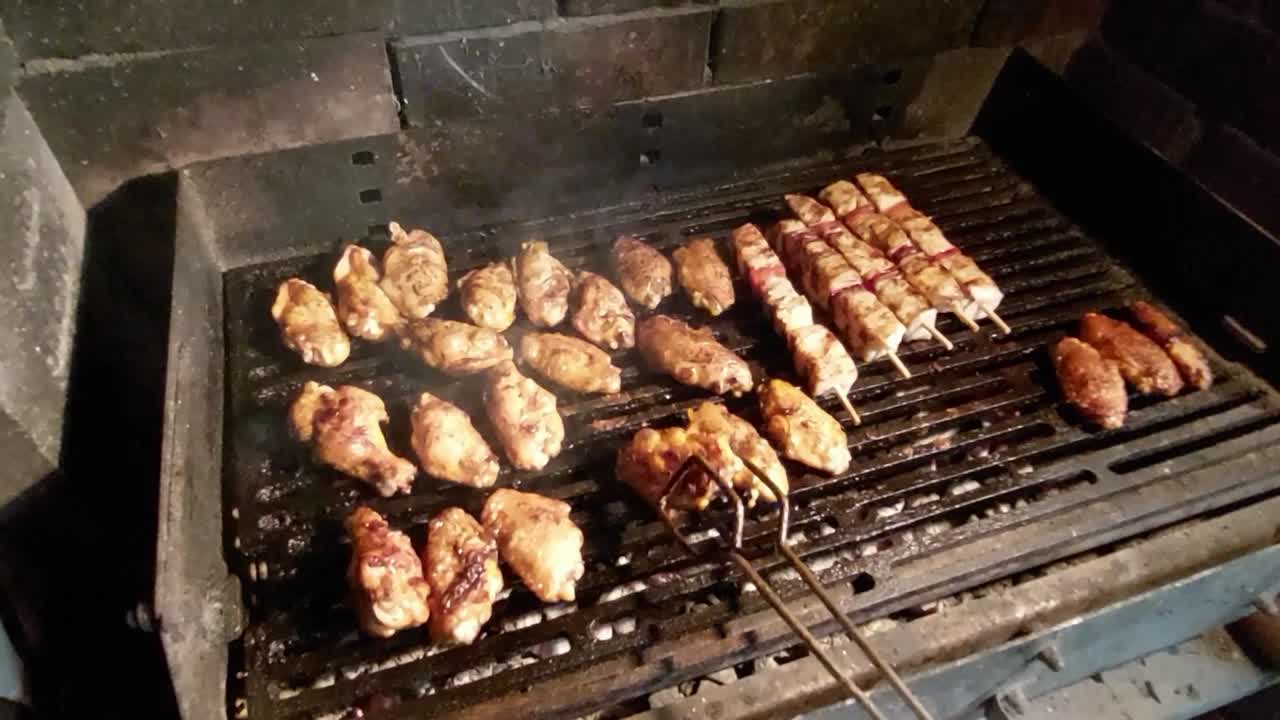mano masculina con tangas girando y arreglando alitas de pollo asando en una barbacoa de carbón caliente