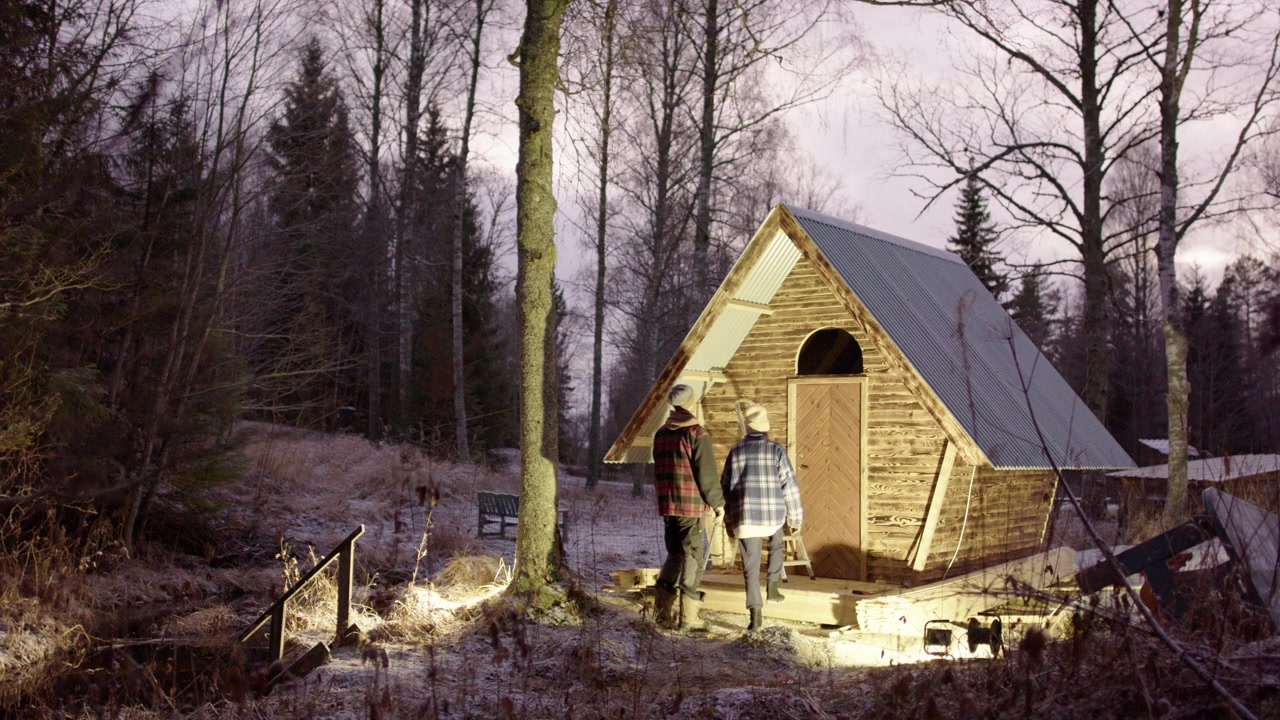 Un couple inspecte les caractéristiques structurelles d'une mini-maison autonome dans les bois à la lumière d'un projecteur.