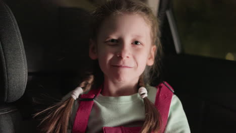 a close view of a child playfully touching her hair and looking directly at the camera while seated in a car