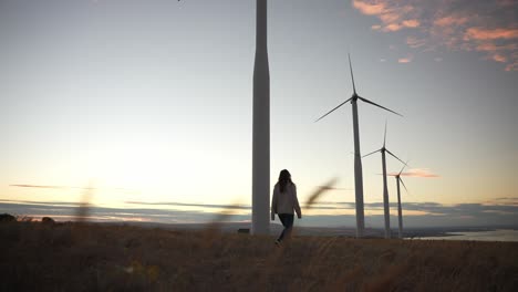 woman walking towards wind turbines at sunset
