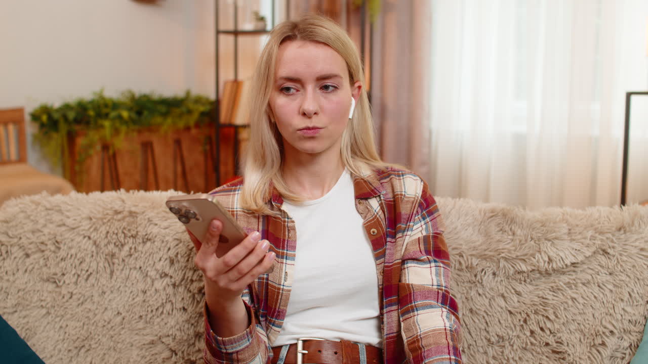 Adult woman listening to voice message with wireless earphones at home surprised by what she hears