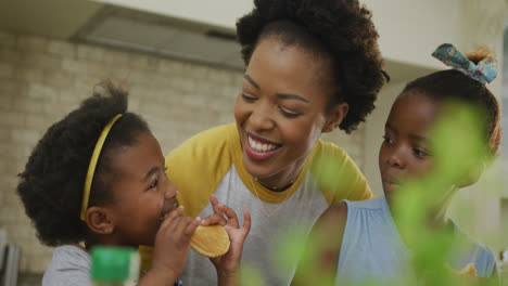 Happy-african-american-mother-with-daughters-eating-in-kitchen