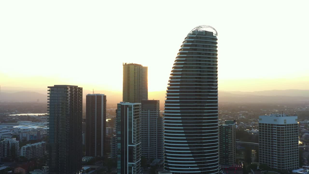 disparo aéreo de aviones no tripulados capturando apartamentos frente al mar y hoteles turísticos en broadbeach, paisaje urbano al atardecer con un hermoso sol asomando a través de los edificios de gran altura, gold coast, queensland