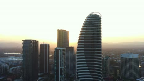 aerial drone shot capturing waterfront apartments and resort hotels at broadbeach, sunset cityscape with beautiful sun peeking through the high rise buildings, gold coast, queensland