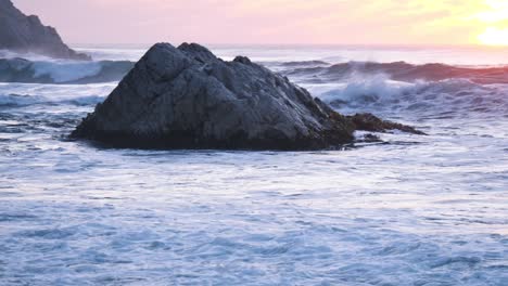 Wellen,-Die-Auf-Einem-Felsen-Mit-Dem-Sonnenuntergang-Im-Hintergrund-Zerquetschen