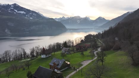 the beauty of walensee region from a drone's perspective, capturing the serenity of lakeside homes, meandering rivers, and majestic snowy peaks under the glowing sunrise