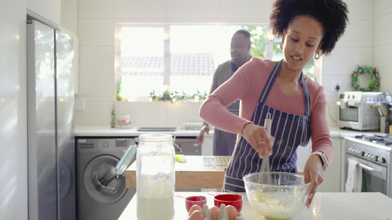 After egg cracking couple whisking batter in bowl at island as man fetching dairy from refrigerator