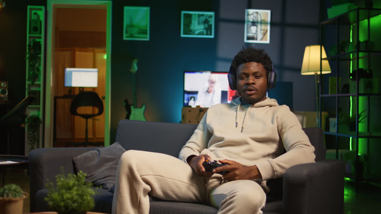 Bored guy plays online video game and spamming attack buttons on his controller, modern loft apartment. Gamer in neon lit space participating in internet e sports competition. Camera B.