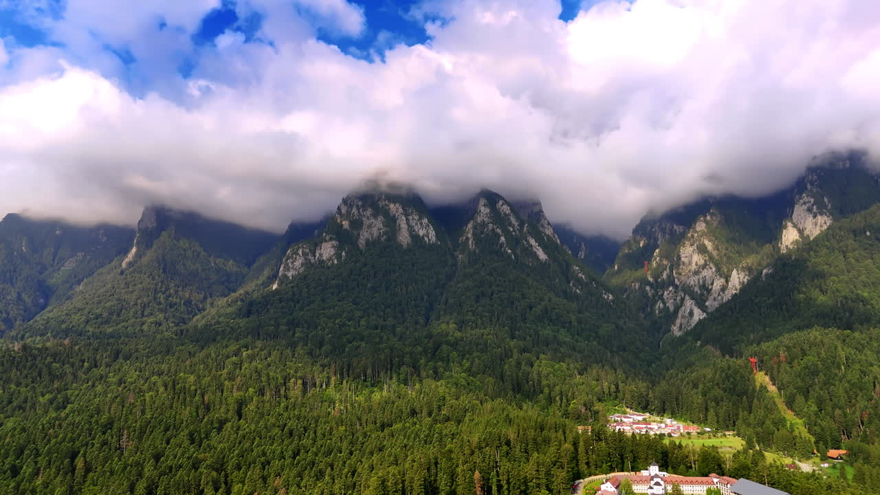 Montagne coperte di nuvole sopra alberi verdi in una valle durante il giorno. La foresta verde si estende verso le alte montagne sotto cieli nuvolosi in una scena di valle