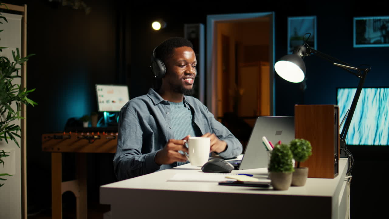 Giovane uomo casual che ascolta un podcast mentre lavora come freelance da casa.