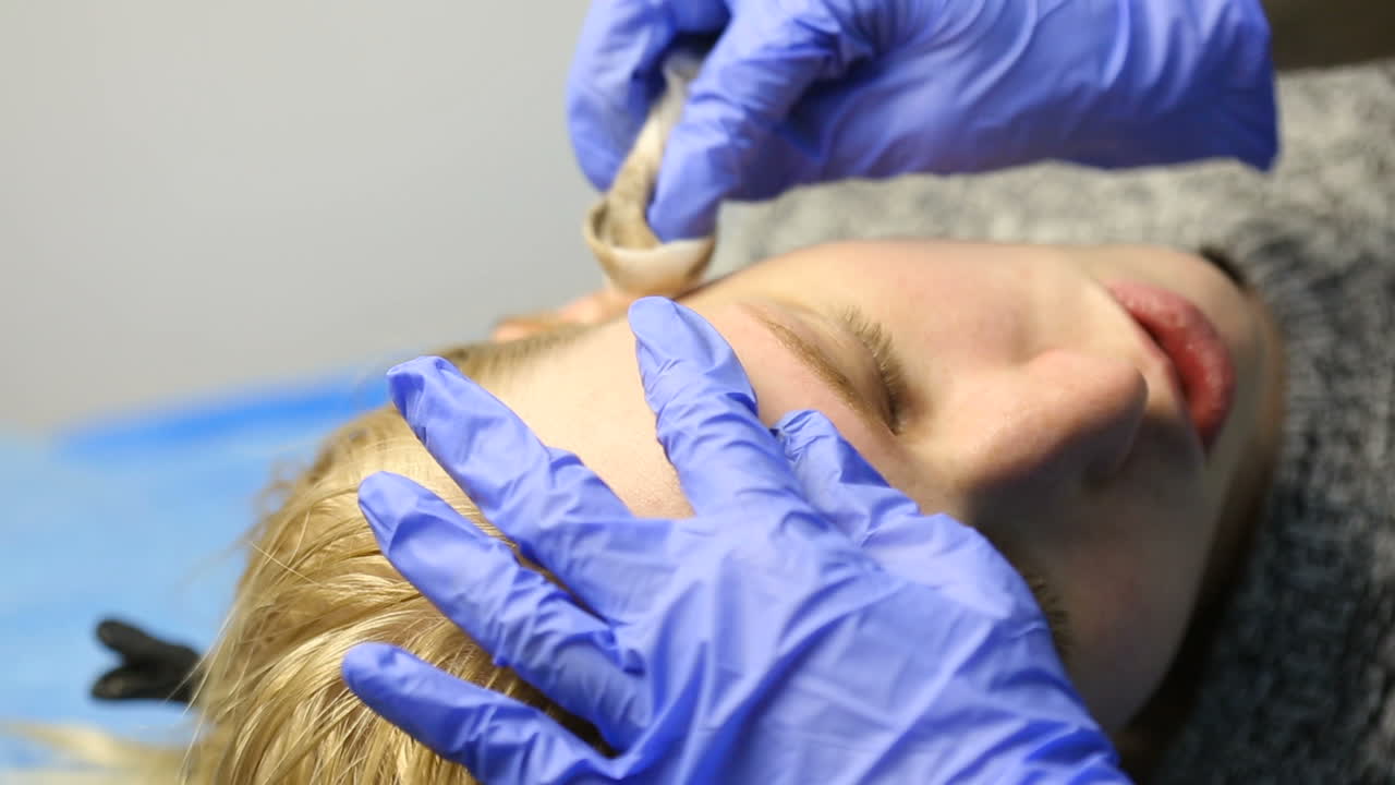 Beautician doing eyebrow tattooing for female face