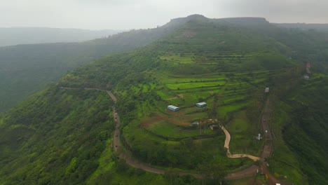 an aerial view of a ghat road in panchgani, maharashtra, shows vehicles driving through lush green mountains under a dramatic monsoon sky, capturing the vibrant aura of the season 4k