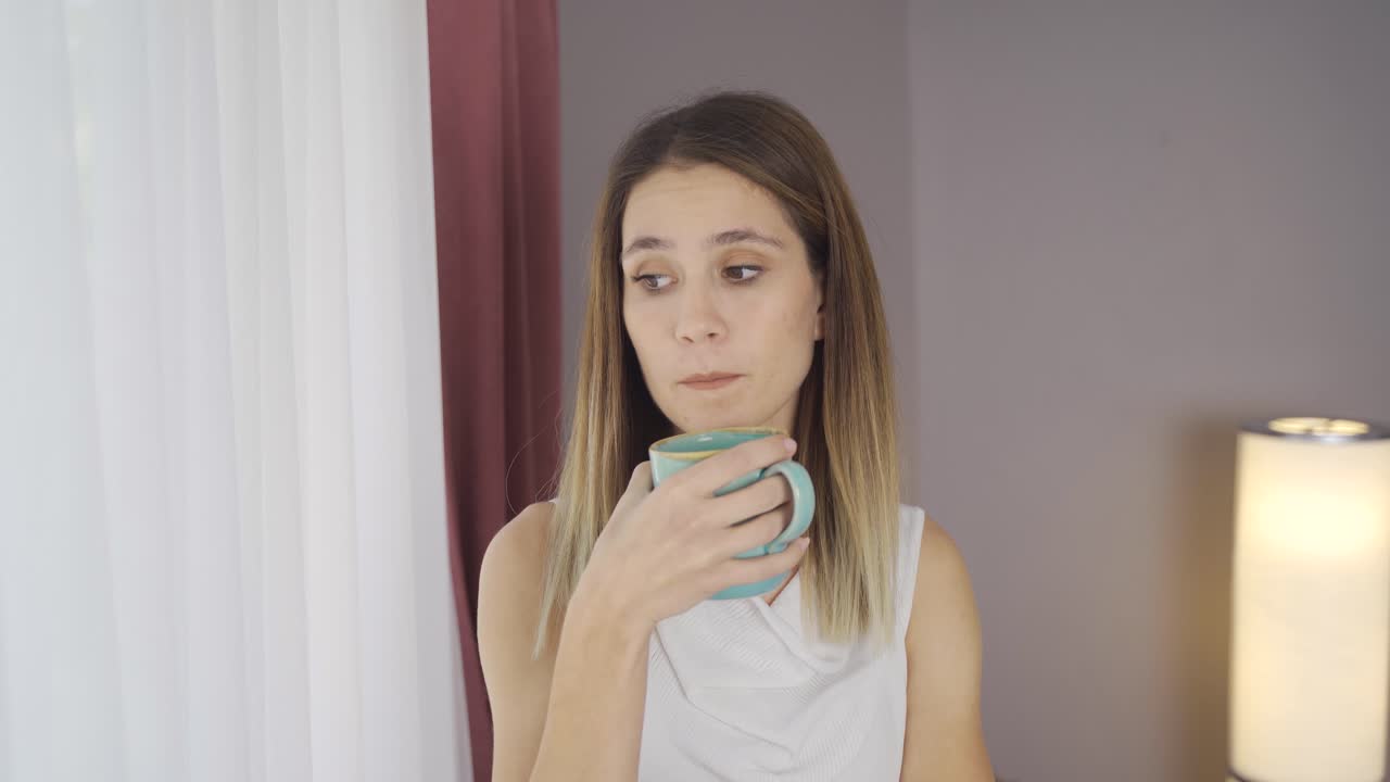 вдумчивая женщина у окна дома пьет кофе.