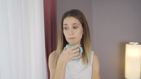 thoughtful woman by the window at home drinks coffee.